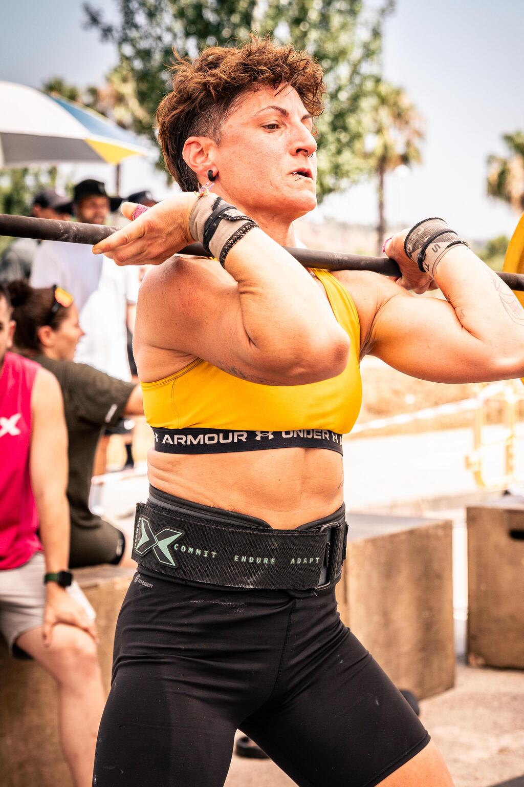Miriam Gómez sosteniendo una barra cargada en posición de front rack durante una competición de CrossFit al aire libre
